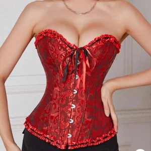 Röd korsett med snörning och volang - Säljer även i xs!! Säljer en snygg röd korsett med svarta detaljer och mönstrad yta. Toppen har snörning framtill, volangkant upptill. 