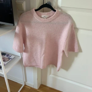 Ljusrosa stickad tröja Gina Tricot XS - Superfin ljusrosa stickad tröja från Gina Tricot i ullblandning. Tröjan har korta ärmar, rund halsringning och en mjuk, fluffig känsla. Perfekt för lager-på-lager och ger en söt vibe till din outfit.