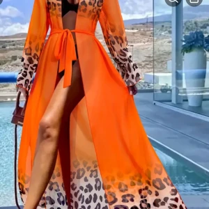 Orange långklänning med leopardmönster - Snygg och transparent orange kaftan/ långklänning med leopardmönster på ärmar, axlar och nederkant. Klänningen har lång ärm, knytband i midjan och en djup slits framtill. Perfekt för att sticka ut vid poolen eller på sommarens event. One size