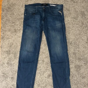 Replay Anbass jeans blå herr - Snygga blå Replay Anbass jeans med klassisk femficksdesign och diskret Replay-märke på bakfickan. Jeansen har en rak passform och är tillverkade i mjukt denim med lätt tvättad look. Perfekta för dig som gillar stilrena och bekväma jeans.