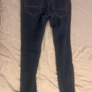 Mörkblå jeans från Hollister W30 L32 - Snygga mörkblå jeans från Hollister med klassisk femficksdesign och kontrastsömmar. Modellen har rak passform och är tillverkad i slitstarkt denim med autentisk känsla. Perfekt för dig som gillar en enkel och stilren look.