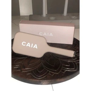 Beige paddleborste från CAIA - Snygg och stilren paddleborste från CAIA i beige med svart borst. Borsten har en bred, platt form och är perfekt för att reda ut håret utan att slita. Handtaget är ergonomiskt och borsten kommer i originalförpackning med CAIA-logga.