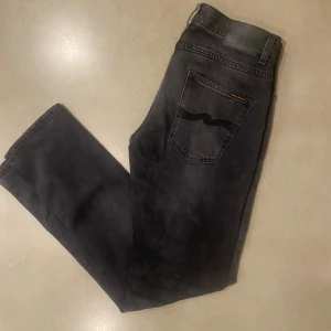 Svarta jeans från Nudie Jeans - Snygga svarta jeans från Nudie Jeans med klassisk femficksdesign och broderad bakficka. Jeansen har raka ben, normal passform och är tillverkade i slitstarkt bomullsmaterial. Perfekt för dig som gillar stilrena och tidlösa jeans.