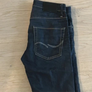 Jack & Jones  mörkblå jeans slim fit - Snygga mörkblà jeans från Jack & Jones med kontrastsömmar och klassisk femficksdesign. Jeansen har raka ben och normal passform, tillverkade i slitstarkt denim med diskret logga pả bakfickan. Perfekta för en stilren och avslappnad look. W32/32 DET ÄR JACK&Jones har ändrat men de ändras inte i annonsen