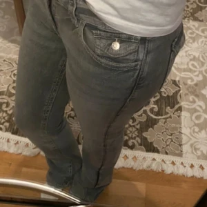 Grå bootcut jeans med fickdetaljer - Säljer ett par grå jeans med snygga fickdetaljer både fram och bak. Modellen har bootcut-ben . Jeansen är från gina