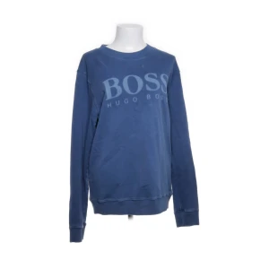 Blå sweatshirt från Hugo Boss - Snygg blå sweatshirt från Hugo Boss med stort BOSS-tryck på bröstet. Tröjan har rund hals, långa ärmar och ribbade muddar vid ärmslut och nederkant. Perfekt för en chill och stilren look.