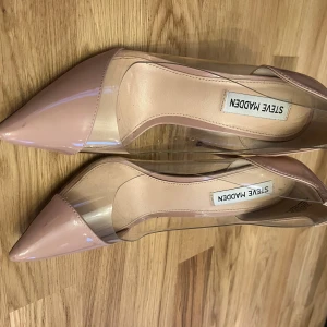 Steve Madden pumps med transparent detalj - Snygga pumps från Steve Madden i ljusrosa lack med transparenta paneler på sidorna. Skorna har spetsig tå och hög smal klack som ger en riktigt chic vibe. Perfekta för dig som gillar att sticka ut med stilrena detaljer och modern design.