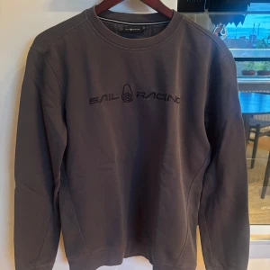 Mörkgrå Sail Racing sweatshirt M - Snygg mörkgrå sweatshirt från Sail Racing i storlek M. Tröjan har rund halsringning, broderad logga framtill och är tillverkad i mjuk bomullsmix. Perfekt för dig som gillar stilrena och sportiga plagg med en clean look.