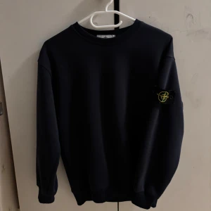 Svart Stone Island sweatshirt - Säljer en svart sweatshirt från Stone Island med klassisk patch på vänster ärm. Tröjan har rund halsringning, ribbade muddar och en clean, stilren look. Perfekt för dig som gillar streetwear och vill ha något enkelt men ändå ikoniskt.