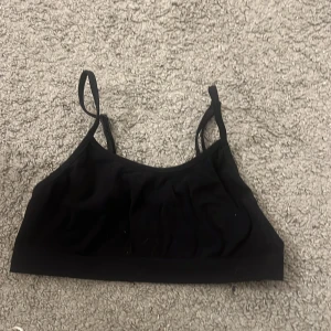 Svart linnetopp från Kappa - Svart linnetopp från Kappa med smala axelband och enkel, stilren design. Tillverkad i mjuk polyester som känns skön mot huden. Perfekt för dig som gillar sportiga och minimalistiska plagg. Säljes i storlek 146/152.