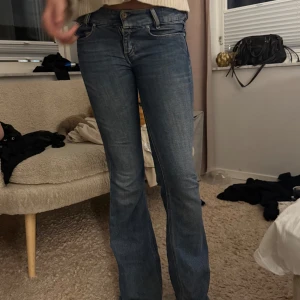 Diesel Louvely bootcut jeans blå W27 L32 - Snygga blå jeans från Diesel, modell Louvely. Klassisk femficksdesign med gul kontrastsöm och bootcut-ben som ger en schysst siluett. Jeansen har normal passform och är tillverkade i slitstarkt denim. Perfekt för dig som gillar en tidlös look med lite edge.