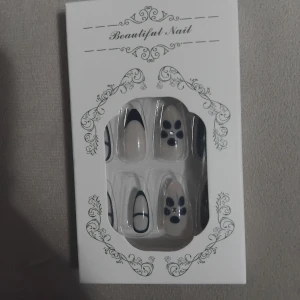 Mörkblå och vit press-on nagelkit - Snyggt set med långa, mandelformade press-on naglar i mörkblått och vitt. Innehåller olika designer: fransk tipp, helblå och naglar med blommönster och små stenar. Kommer med nagelfil och klisterlappar för enkel applicering. Har bara använt några finns 19 kvar i.