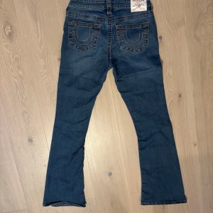 True Religion BECCA Mid Rise Bootcut Jeans - Snygga mörkblå jeans från True Religion, modell BECCA med midwaist och bootcut. Klassiska femficksjeans med orange kontrastsömmar och ikoniska bakfickor med broderad logga. 