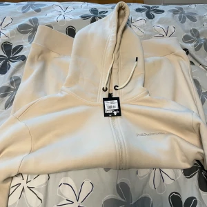 Beige zip up från Peak Performance XL - Helt ny och aldrig anvand Peak Performance zip up med lapp kvar som var en födelsedagspresent och köpt i Peak Performace butiken. Säljer på grund av för stor storlek och fel stil då den inte går att lämnas tillbaka utan kvitto. Storlek XL (herr) och färg Sand fog. Nypris i butik: 1400 kr. Har en fläck som fanns där sen innan som säkert går bort om du tvättar den men kan inte lova något då jag inte vet vad fläcken kom ifrån.
