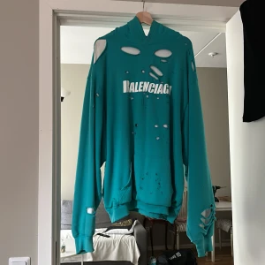 Turkos oversized hoodie från Balenciaga - Cool turkos hoodie från Balenciaga med distressed look och stora slitningar över hela tröjan. Extremt oversized passform då jag som 188cm lång man nästan drunknar i den. Perfekt statement-plagg för dig som gillar streetwear och vågar sticka ut.