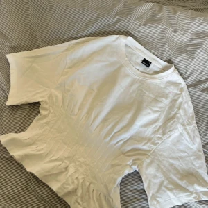 Vit croppad t-shirt från Gina Tricot - Säljer en vit t-shirt från Gina Tricot i storlek M. Modellen är croppad med korta ärmar och har snygga sömdetaljer framtill som ger en cool look. Materialet är mjuk bomull och passformen är loose. Perfekt till jeans eller kjol!