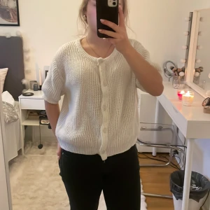 Vit stickad kofta med knappar - Säljer en vit stickad kofta med rund hals och korta ärmar. Koftan har ribbade muddar och knappar framtill. Storleken är L, som referens så brukar jag ha s på tröjor.