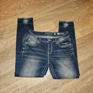 Miss Me jeans med broderi - Snygga blå jeans från Miss Me med broderade bakfickor i zigzag-mönster och små nitar. Jeansen har fransade benslut, kontrastsömmar och en midwaist passform. 