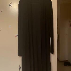 Svart lång cardigan jacka Boohoo - Svart lång cardigan jacka från Boohoo i storlek XL. Jackan har en enkel och stilren design med lång ärm och öppen framtill. Materialet är mjukt och lätt, perfekt för lager-på-lager och chill stil. Passar dig som gillar minimalistiskt och comfy.