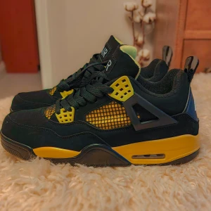 Helt nya Nike Air Jordan 4 svart/gul Sneakers 43 - Säljer ett par aldrig använda Nike Air Jordan 4 sneakers i svart och gul färg. Skorna har klassisk mesh och detaljer i gult, svarta snören och en robust sula. Ovandelen är i mocka och syntet, med ikonisk AIR-logga på plösen. 