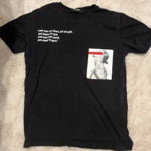 Svart t-shirt från Dsquared2 med print - Svart t-shirt från Dsquared2 med vit text på bröstet och en stor grafisk print med röd detalj på framsidan. T-shirten har rund hals och är tillverkad i mjuk bomull. Perfekt för dig som gillar statement-plagg och streetstyle.