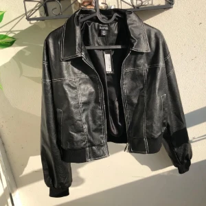 Svart skinnjacka från Boohoo - Snygg svart skinnjacka från Boohoo med vita kontrastsömmar och dragkedja framtill. Jackan har en klassisk krage, ribbade muddar och en lite oversized passform och vattentät. Jag råkade köpa två likadana så därför är det två likadana annonser i min profil.