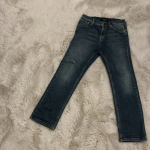 Replay blå jeans Thad straight fit - Snygga blå jeans från Replay, modell Thad med klassisk femficksdesign och raka ben. Jeansen har en mörk tvätt med lätt slitning och kontrastsömmar. Passar dig som gillar en enkel och stilren look med normal passform och midwaist.