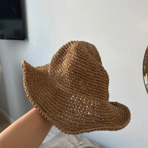 Brun virkad stråhatt med böjd brätte - Säljer en brun virkad stråhatt med böjt brätte som ger en chill och avslappnad vibe. Hatten är tillverkad i ett grovt, luftigt material som passar perfekt för soliga dagar. Den har en klassisk form med lite cowboy-inspirerad look och är lätt att styla till sommaroutfits.