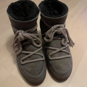 Bruna Inuikii moon boots med snörning - Säljer ett par bruna Inuikii moon boots med grov snörning och rund tå. Utsidan är i mocka och insidan är fodrad med mjuk päls för extra värme. Snyggt robust utseende och platt sula, perfekta för kalla vinterdagar.