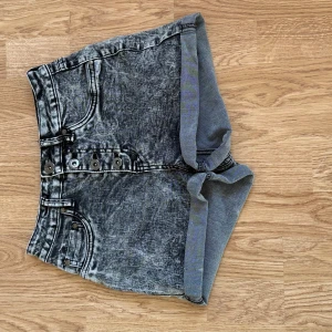 Grå högmidjade jeansshorts med knappar - Snygga grå jeansshorts med tvättad look och hög midja. Framtill finns flera knappar och klassiska fickor, medan baksidan har två stora bakfickor. Shortsen har uppvikta ben och en loose passform som ger en chill vibe.