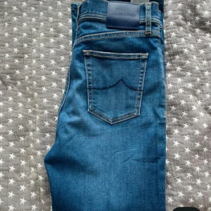 Blå jeans från Jacob Cohen, storlek 28 - Snygga blå jeans från Jacob Cohen i klassisk femficksmodell. Jeansen har en mörkblå ton med kontrastsömmar och exklusiva detaljer som broderad insida och etikett i skinn. Tillverkade av italienska tyger för extra komfort och stil.