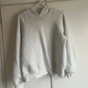 Ljusgrå hoodie med huva - Enkel och stilren ljusgrå hoodie med huva och långa ärmar. Tröjan har en relaxed passform och ribbade muddar vid ärmslut och nederkant. Perfekt för chill dagar eller när du vill ha något bekvämt på dig.