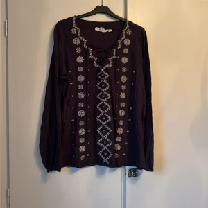 Mörkblå broderad blus från L.O.G.G. - Säljer en mörkblå blus från L.O.G.G. med snygga vita broderier framtill och runt halsen. Blusen har lång ärm, v-ringad hals med snörning och är gjord i mjuk bomull. Perfekt för dig som gillar boho-vibe och detaljer.