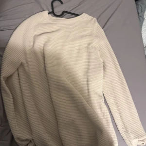 Beige ribbad stickad tröja - Säljer en beige stickad tröja med ribbad struktur och lång ärm. Perfekt för lager-på-lager och enkel att matcha med olika outfits. Tröjan har en klassisk rund halsringning och en avslappnad passform.