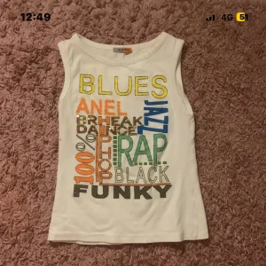 Vit linnetopp med färgglad text från Anel - Säljer en vit linnetopp från Anel med coolt tryck i flera färger och olika musikgenrer som BLUES, JAZZ, RAP och FUNKY. Toppen är ärmlös och har en rund halsringning. Perfekt för dig som gillar streetstyle och färgglada detaljer.