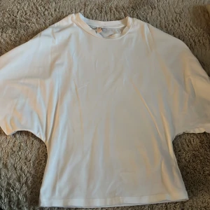 Vit oversized topp från Nelly - Vit oversized topp från Nelly i mjuk bomull. T-shirten har rund halsringning och breda, lösa ärmar för en avslappnad look. Perfekt att styla med jeans eller kjol för en enkel och clean outfit.