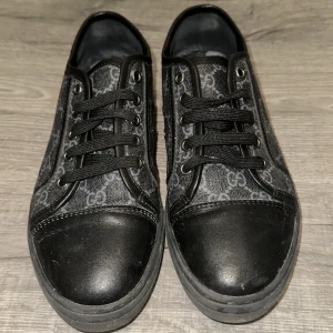 Gucci monogram skor  - Pris ej hugget i sten 🪨.Snygga svarta sneakers från Gucci med klassiskt GG-mönster i grått. Skorna har svarta skinnpartier vid tå och häl, svarta snören och detaljer i metall. Yttersulan är i svart gummi med Gucci-logga undertill. Perfekta för dig som vill ha en lyxig och stilren look.