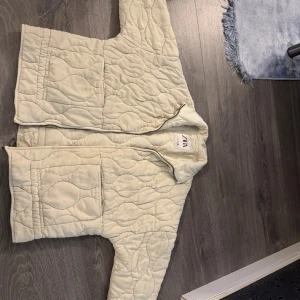 Quiltad beige jacka från ZARA - Säljer en quiltad beige jacka från ZARA i storlek S. Jackan har ett vågigt mönster, två stora fickor framtill och dragkedja. Den har en loose passform och är långärmad, perfekt för dig som gillar chill och stilren vibe.