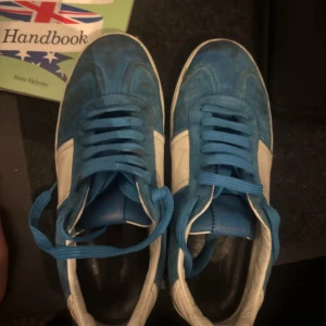 Valentino Rockstud blå sneakers - Snygga Valentino Rockstud sneakers i blå mocka med vita detaljer och platt sula. Skorna har blå snörning och coola nitar på hälen som ger extra edge. Perfekt för dig som gillar exklusiva märken och vill sticka ut med din stil.