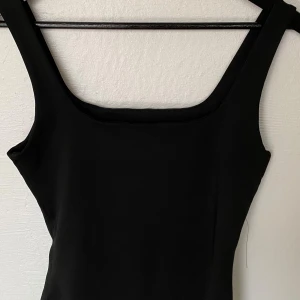 Svart linnetopp från SHEIN - En stilren svart linnetopp från SHEIN med breda axelband och fyrkantig urringning. Toppen är enkel och tight i modellen, perfekt att matcha med jeans eller kjol. Materialet är mjukt och stretchigt för en bekväm passform.