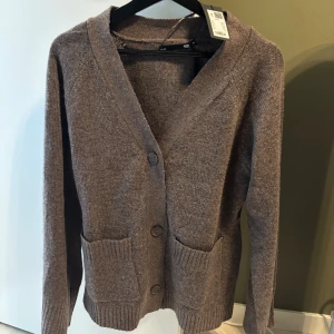 Brun kofta från 157 med fickor - Mysig brun kofta från 157 med stora ribbade fickor framtill och knappar hela vägen. Perfekt för lager-på-lager och har en klassisk v-ringad design med lång ärm. Enkel att matcha till det mesta och superbekväm. Slutsåld 