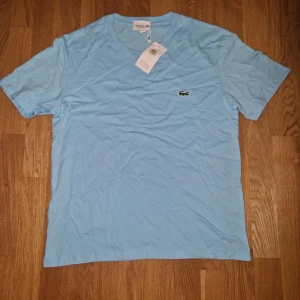 Ljusblå t-shirt från Lacoste - Snygg ljusblå t-shirt från Lacoste med klassisk krokodillogga broderad på bröstet. T-shirten har rund halsringning och är tillverkad i mjuk bomull. Perfekt för en avslappnad och stilren look.