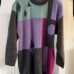 Färgglad stickad tröja med grafiskt mönster - Unik stickad tröja med coolt grafiskt mönster i lila, grått, mintgrönt och mörkrosa. Tröjan har långärmade och loose passform, med olika former som cirklar och trianglar på framsidan. Perfekt för dig som gillar färg och statement-plagg.