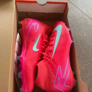 Nike Superfly 10 Pro FG fotbollsskor - Säljer ett par Nike Superfly 10 Pro FG fotbollsskor i en riktigt snygg och iögonfallande rosa färg med turkosa detaljer och sula. Skorna har snörning, hög krage och är tillverkade i syntetmaterial för bästa grepp och känsla på planen.