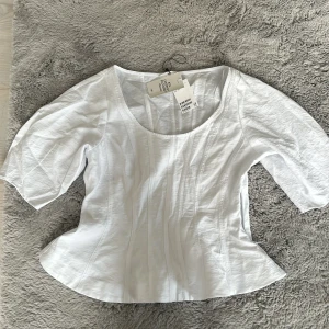 Vit korsett-topp från H&M - Säljer en vit korsett-topp från H&M med snygg rundad halsringning och markerade sömmar som ger en figurnära siluett. Toppen har halvlånga ärmar och är tillverkad av 83% LENZING™ ECOVERO™ viskos för en mjuk och skön känsla.helt ny så aldrig använd