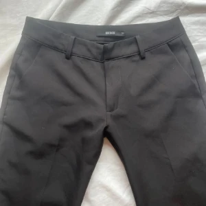 Svarta kostymbyxor från BikBok - Svarta kostymbyxor från BikBok i klassisk rak modell med hällor för bälte och diskreta fickor. Byxorna har dragkedja och knapp framtill och är tillverkade i ett mjukt, vävt material som ger en clean look. Perfekta till en snygg topp eller skjorta.