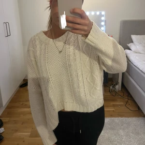 Vit/beige stickad tröja från Gina Tricot - En supermysig vit/beige stickad tröja från Gina Tricot med kabelstickat mönster och ribbade muddar. Tröjan har en loose passform, är croppad och har långa ärmar. Perfekt att slänga på sig när det är kyligt ute. 😊💗