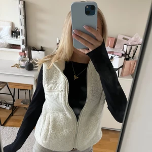 Vit fleeceväst från Lindex - Mysig vit fleeceväst från Lindex med dragkedja framtill och hög krage. Västen har en praktisk bröstficka med dragkedja och två sidofickor. Perfekt att slänga över en hoodie eller långärmad tröja för extra värme. Säljer pga att den inte kommer till användning🥰storlek 134-140 motsvarar typ en xxs. Säljer pga att den inte passar mig💞