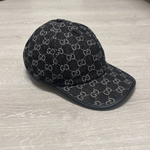 Gucci keps - Snygg keps med klassiskt GG-mönster över hela ytan. Kepsen är tillverkad i jeansmaterial med justerbar rem bak och detaljer i svart läder. Insidan är ljus och har en etikett med Gucci-logga. Perfekt för dig som vill ha en lyxig streetstil.