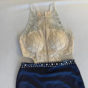 Blå långklänning med glittrig topp - Supersnygg långklänning med marinblå satinkjol och en champagnefärgad topp dekorerad med pärlor och glittriga stenar. Toppen har meshdetaljer och markerad midja med stenar längs linningen. Perfekt för bal eller festkväll!